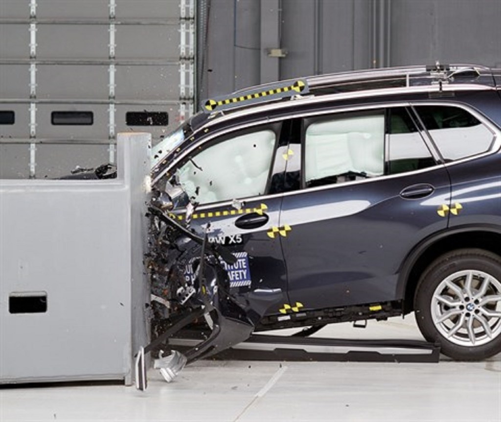 A BMW X5 is being crash tested. The front of the car is smashed into a barrier.