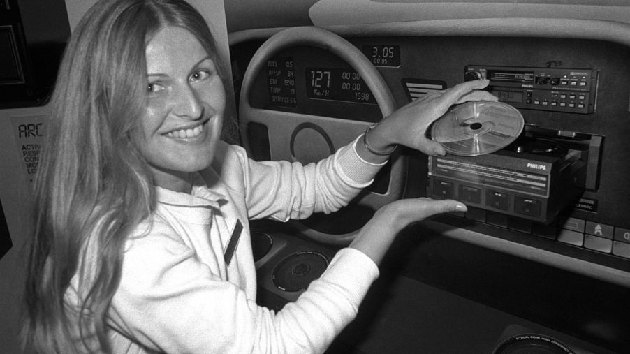 A black and white photo of a woman presenting a CD player in a vehicle