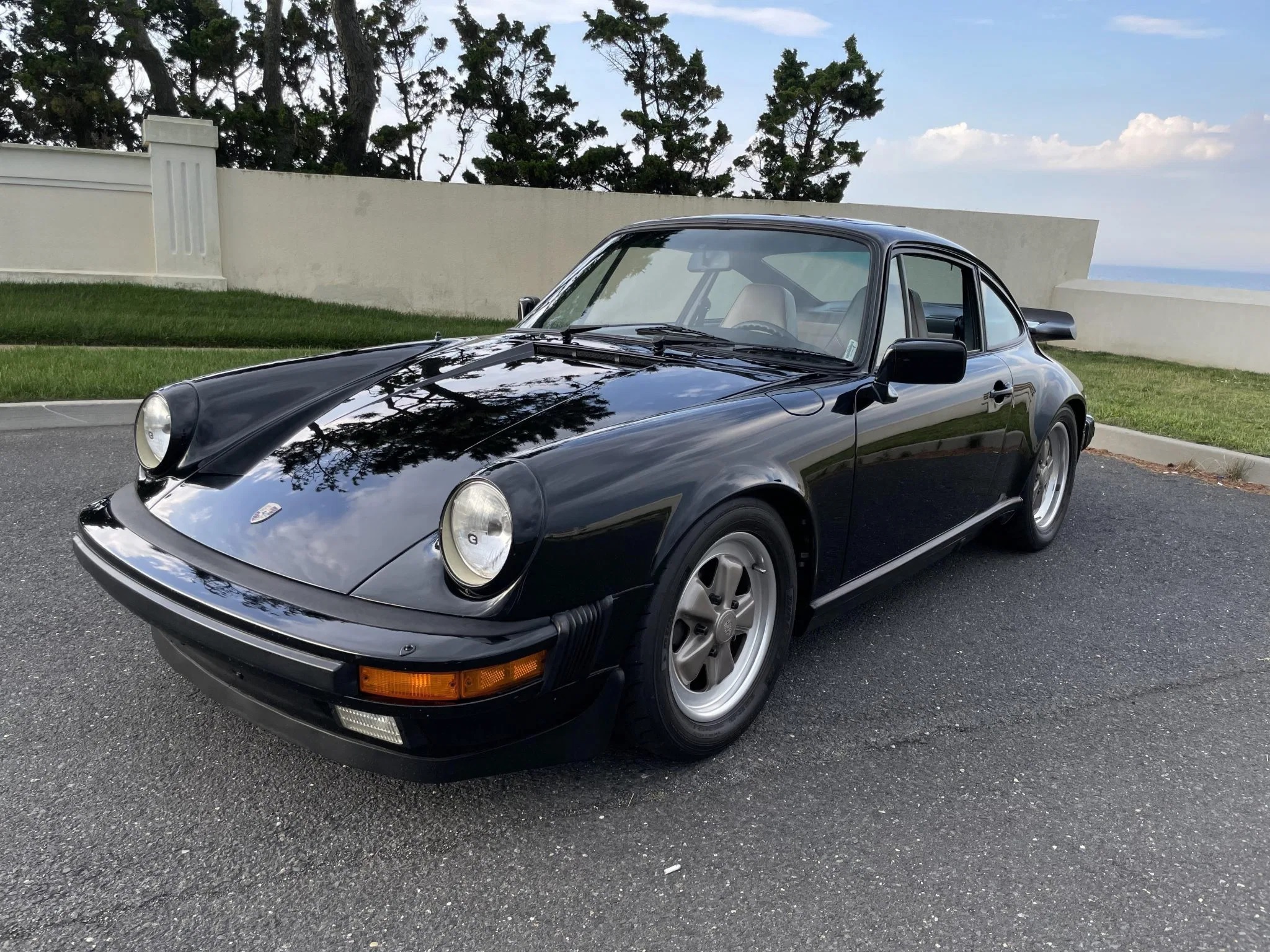 The front 3/4 view of a black 1984 Porsche 911 Carrera 3.2 parked in an oceanside parking lot