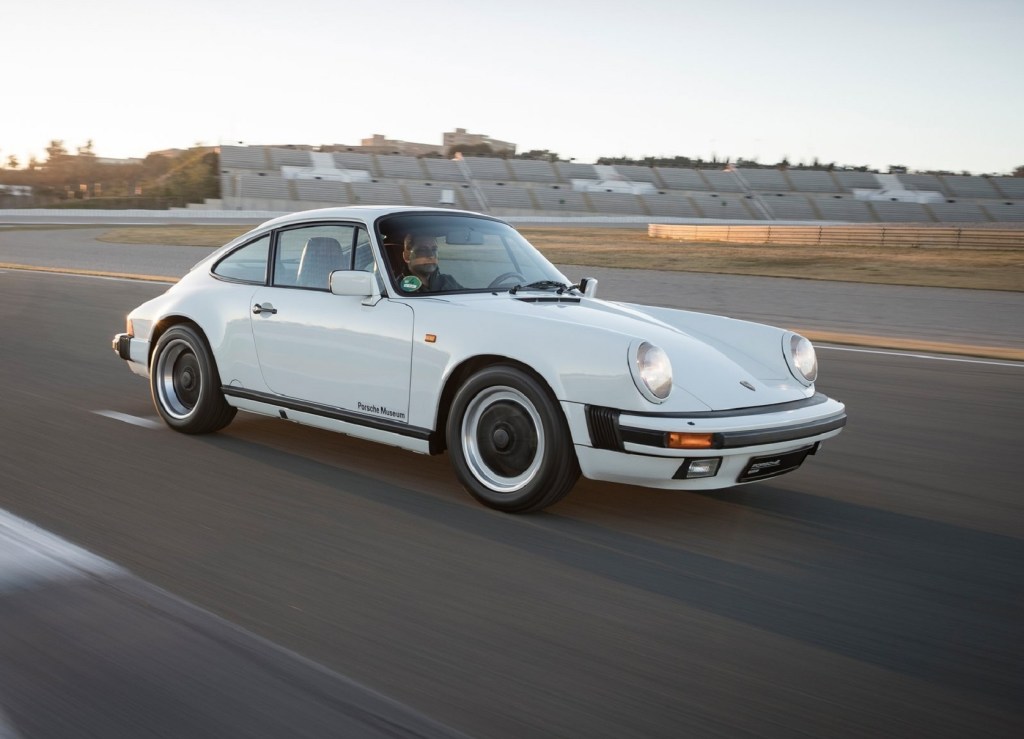 A white 1984 Porsche 911 Carrera 3.2 driving on a desert racetrack