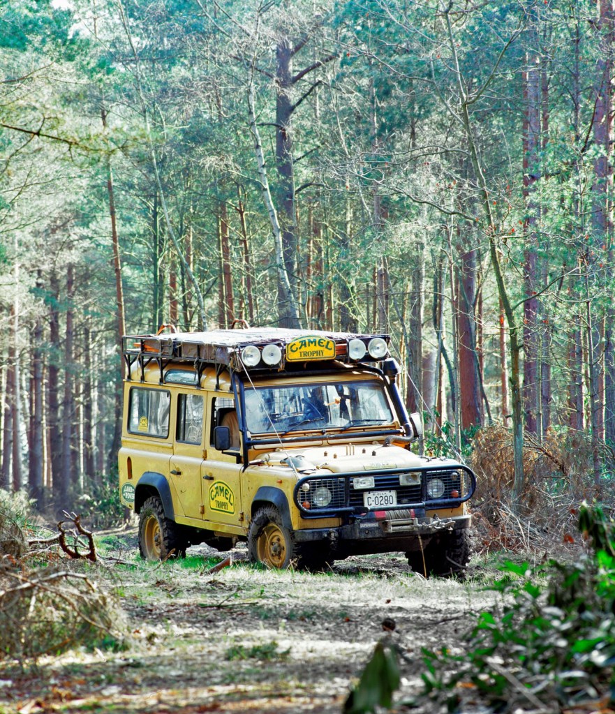 A yellow 1995 Land Rover Defender Camel Trophy in a forest