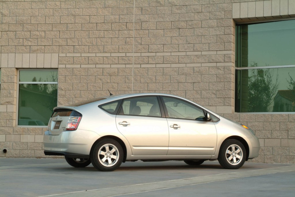 A silver 2004 Toyota Prius hybrid car parked next to a beige brick building