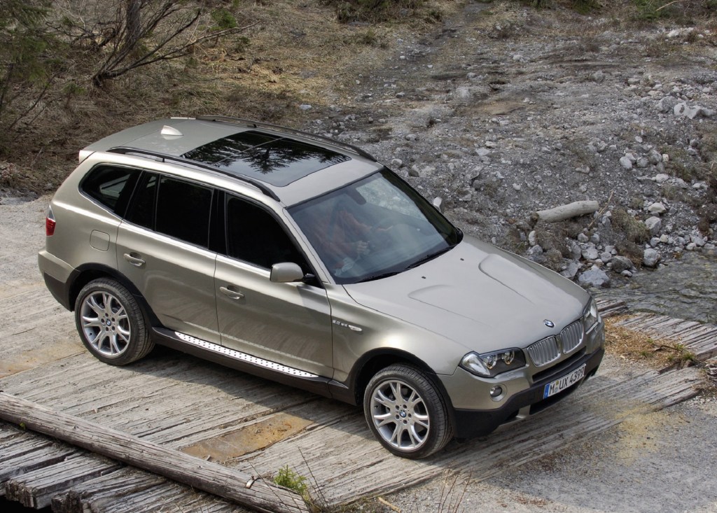 An overhead front 3/4 view of a tan 2007 BMW X3 3.0si crossing a wooden bridge over rocky ground