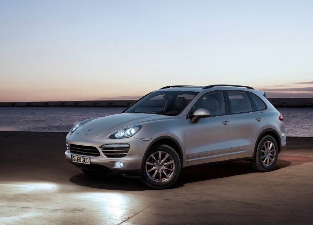A silver '958' 2011 Porsche Cayenne with its lights on by the ocean