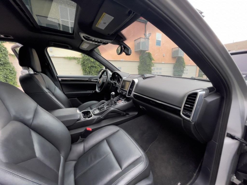 The black-leather-upholstered front seats, dashboard, and sunroof of a 2013 Porsche Cayenne Manual