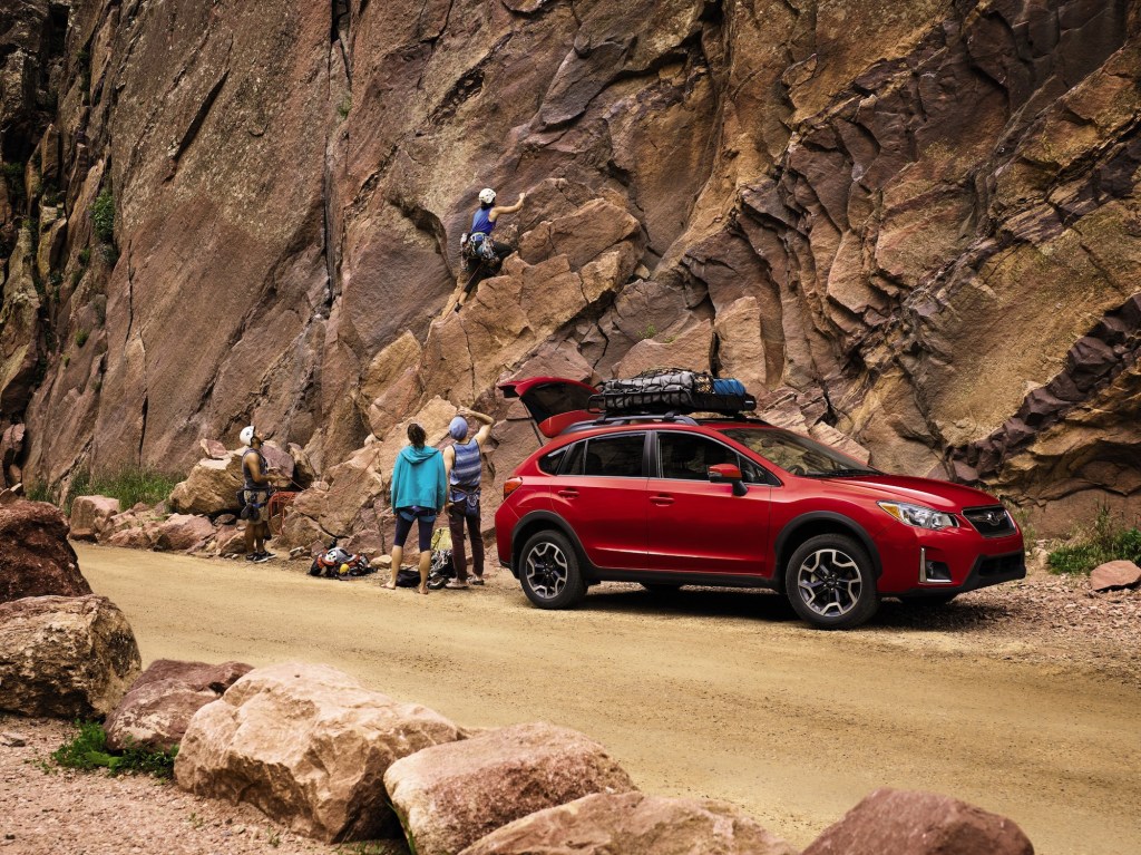 A red 2017 Subaru Crosstrek Special Edition parked at the bottom of a rocky cliff as a climber scales it