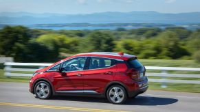 A red 2020 Chevrolet Bolt EV model driving on a highway past a white fence and grass fields