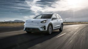 A white 2020 Kia Niro EV driving on a highway on a cloudy day in a plain with one small hill.