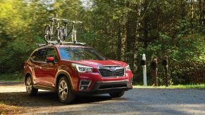 A red 2020 Subaru Forester in a wooded area parked on a dirt road with bicycles on the top rack.