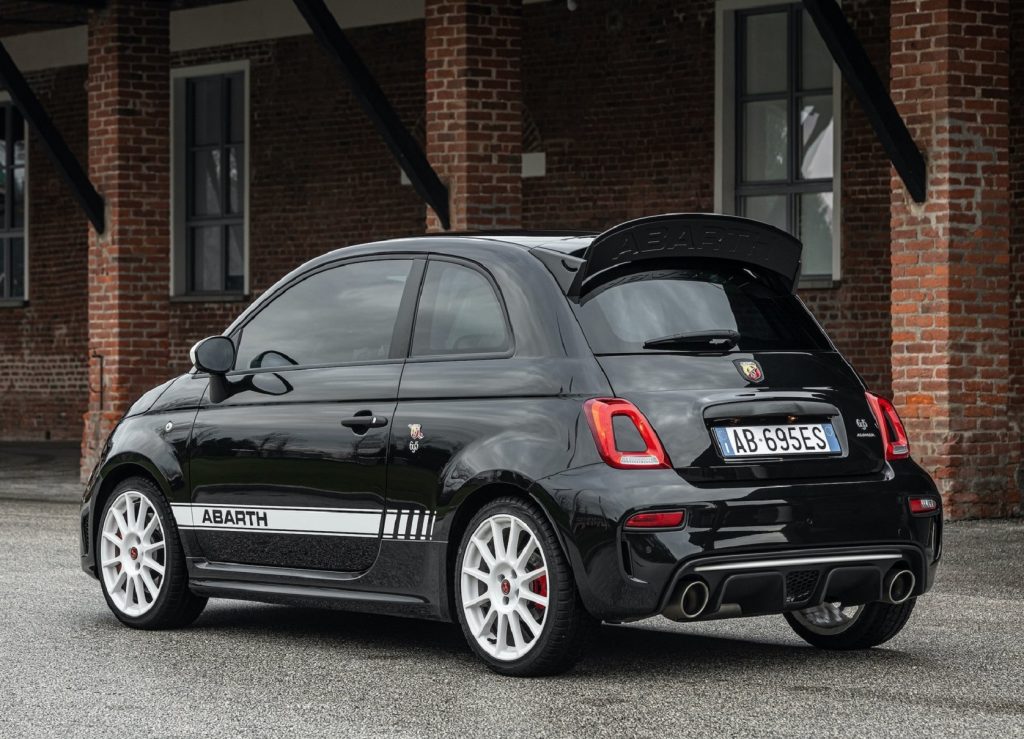 The rear 3/4 view of a black-and-white 2021 Abarth 695 EsseEsse next to a brick building