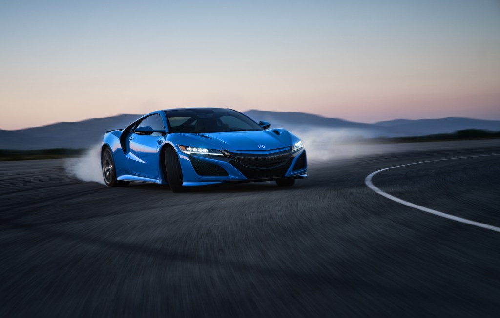 A bright-blue 2021 Acura NSX sports car turns a corner on a track with mountains in the distance