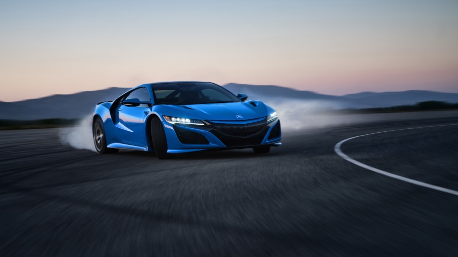 A bright-blue 2021 Acura NSX sports car turns a corner on a track with mountains in the distance