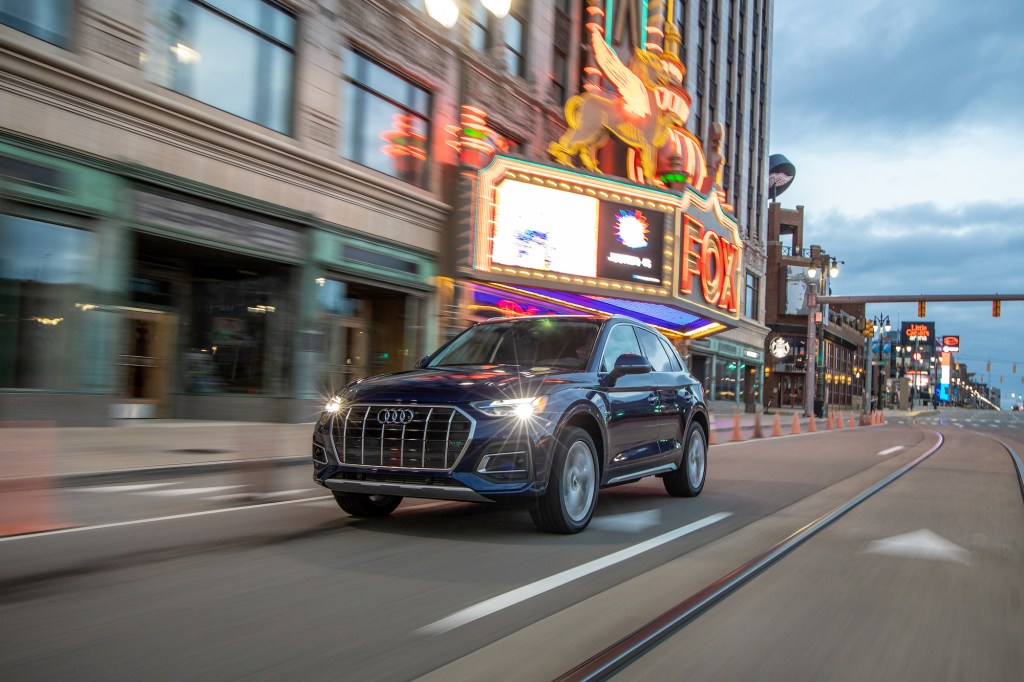 A dark-blue metallic 2021 Audi Q5 traveling on a city street past a theater marquee