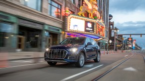 A dark-blue metallic 2021 Audi Q5 traveling on a city street past a theater marquee