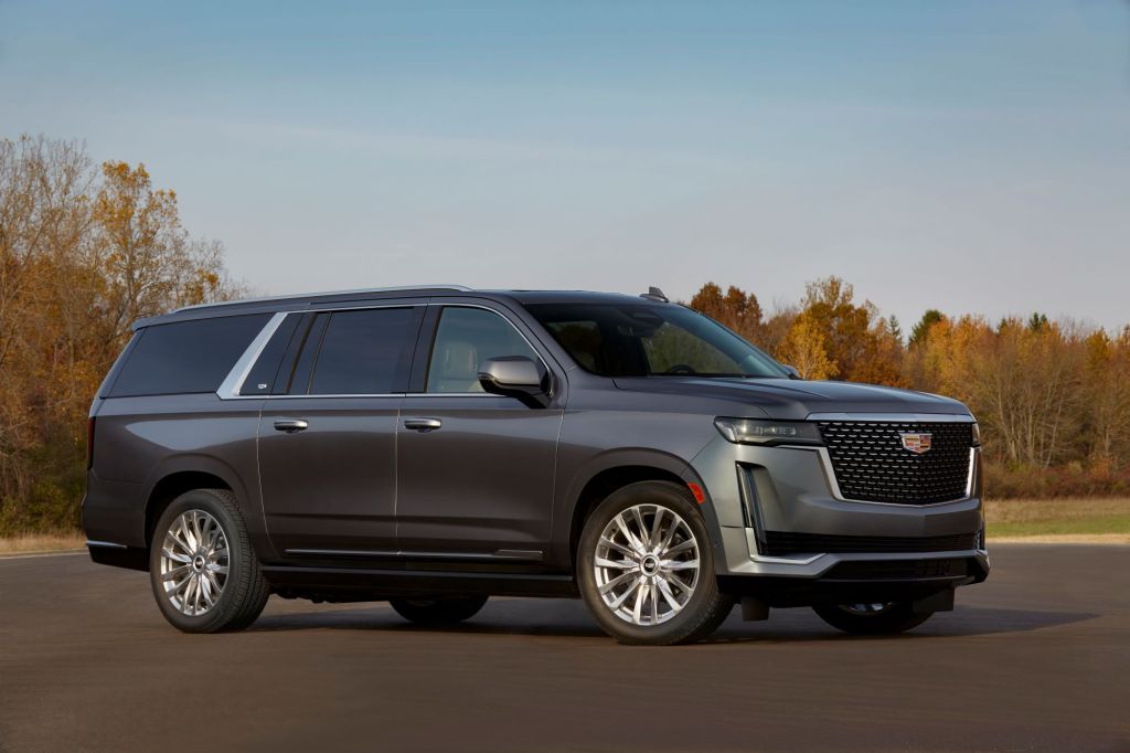 The 2021 Cadillac Escalade full-size SUV with gray metallic paint parked on an asphalt lot near a forest of trees