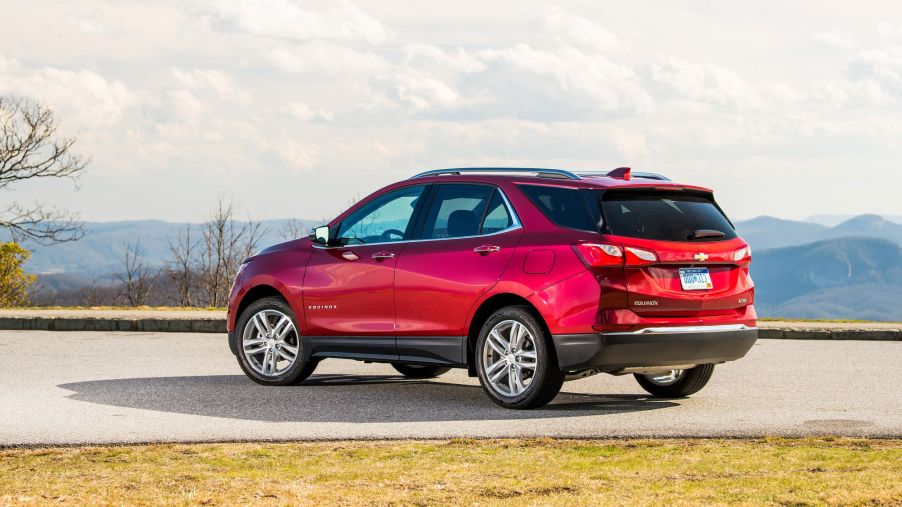 A red 2021 Chevrolet Equinox parked on a concrete drive surrounded by grass with trees and mountains in the background.
