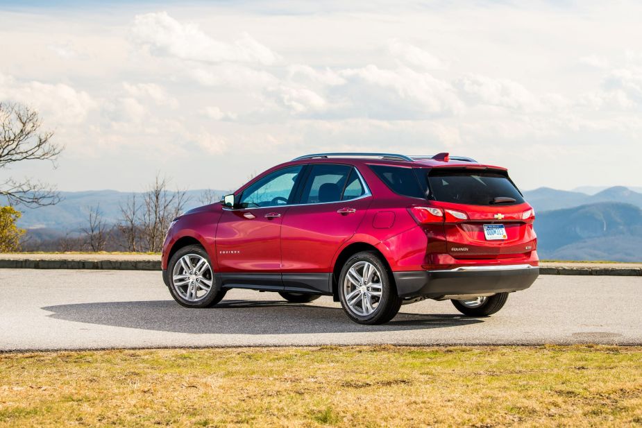 A red 2021 Chevrolet Equinox parked on a concrete driveway surrounded by grass with trees and mountains in the background.