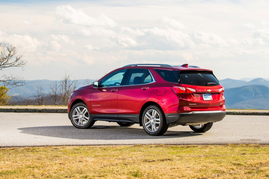 A red 2021 Chevrolet Equinox parked on a concrete drive surrounded by grass with trees and mountains in the background.