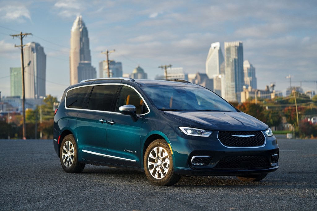 A 2021 Chrysler Pacifica Pinnacle Hybrid minivan in Fathom Blue parked in front of a cityscape