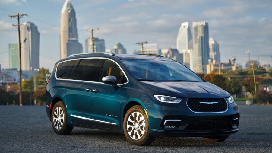 A 2021 Chrysler Pacifica Pinnacle Hybrid minivan in Fathom Blue parked in front of a cityscape