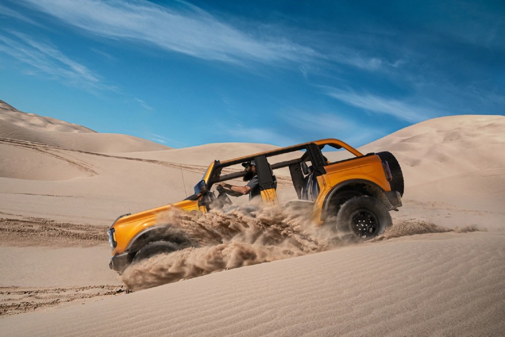 An orange 2021 Ford Bronco Wildtrak 4-door with no doors or roof drives down a desert dune