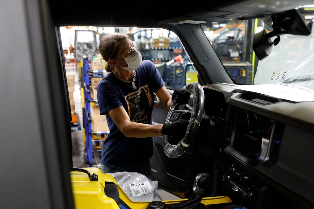 A Ford employee assembles a steering wheel on a 2021 Ford Bronco