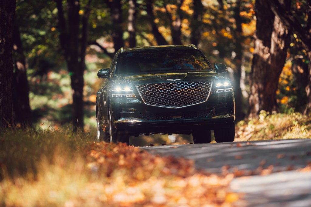 A head-on view of a dark-green 2021 Genesis GV80 luxury SUV with its headlights on in Hudson Valley, New York