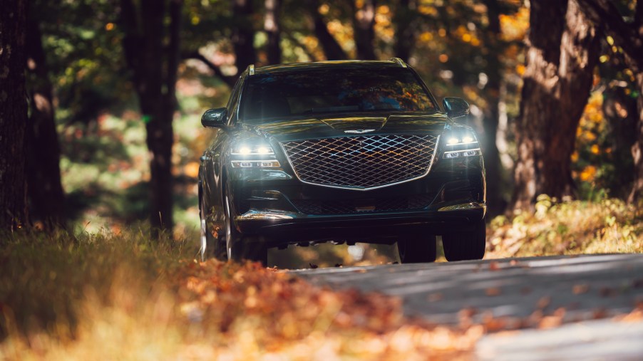 A head-on view of a dark-green 2021 Genesis GV80 luxury SUV with its headlights on in Hudson Valley, New York