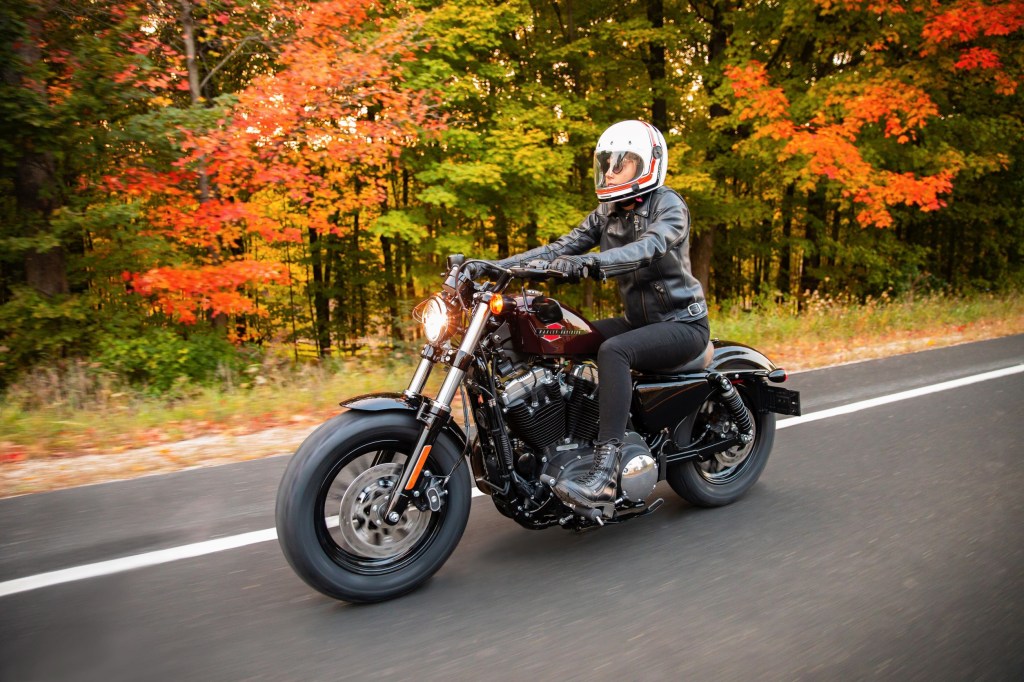 A rider rides a maroon 2021 Harley-Davidson Forty-Eight on a tree-lined road