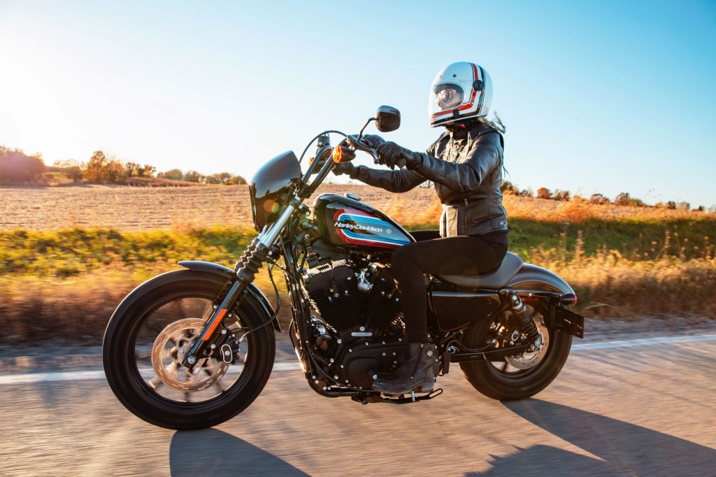 A white-helmeted, black-clad rider on a black 2021 Harley-Davidson Sportster Iron 1200 riding down the road