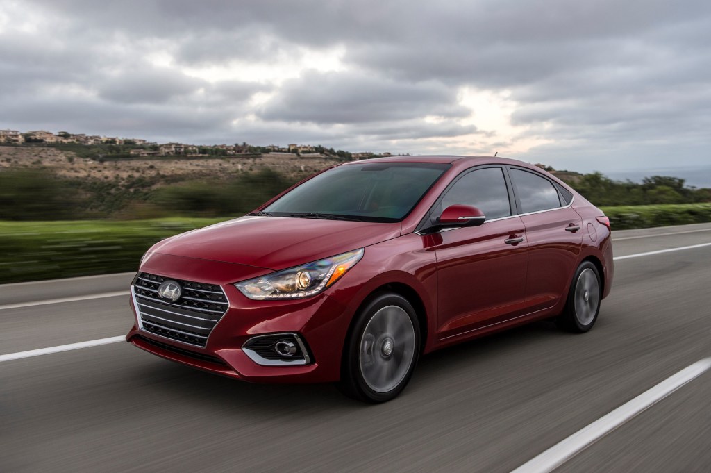 A red metallic 2021 Hyundai Accent traveling on a highway past green grass and hills on a cloudy day