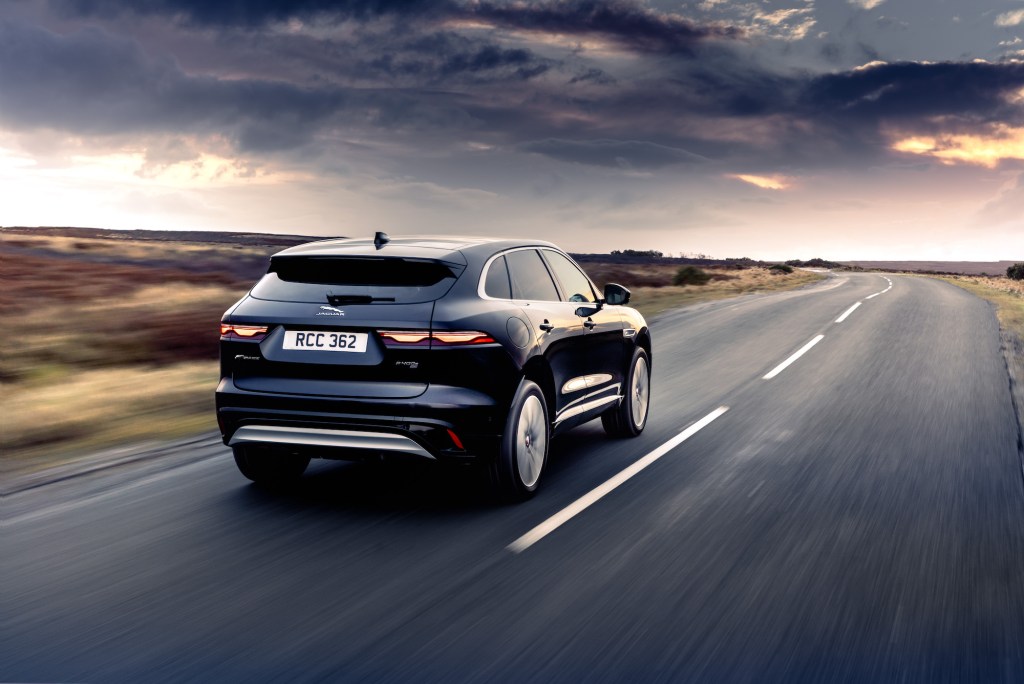 A dark-blue 2021 Jaguar F-Pace luxury compact SUV on a two-lane highway in the country as dark clouds form