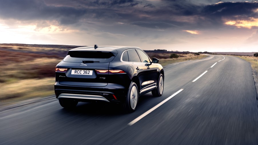 A dark-blue 2021 Jaguar F-Pace luxury compact SUV on a two-lane highway in the country as dark clouds form