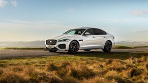 A white 2021 Jaguar XF luxury midsize sedan parked on a road overlooking mountains on a sunny day