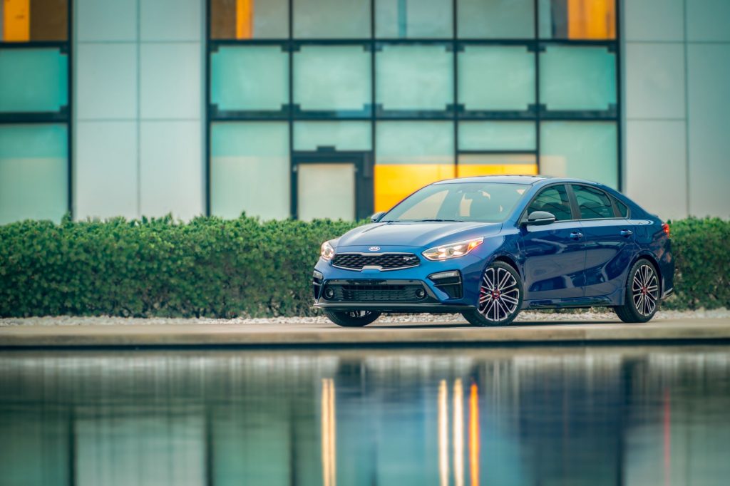 A blue 2021 Kia Forte GT Sport sedan model parked near a pond outside of a dealership