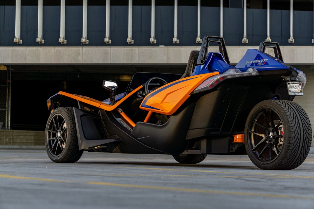 The rear 3/4 view of a blue-and-orange 2021 Polaris Slingshot R in a parking lot