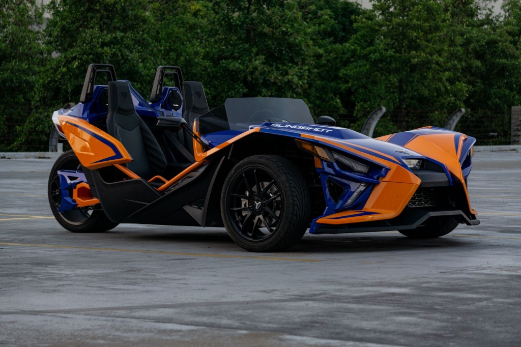 The side 3/4 view of a blue-and-orange 2021 Polaris Slingshot R in a parking lot