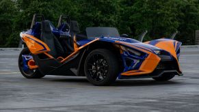 The side 3/4 view of a blue-and-orange 2021 Polaris Slingshot R in a parking lot