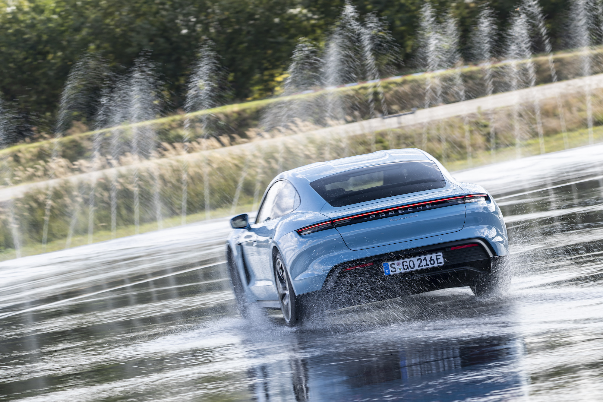 A sky-blue 2021 Porsche Taycan 4S maneuvers on wet pavement as water shoots into the air