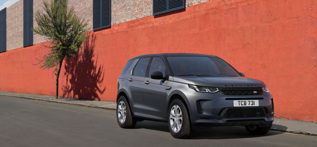 A grey 2021 Range Rover Evoque sits in front of a orange and grey brick building with two windows on a blacktop road.