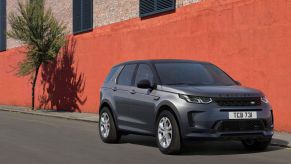 A grey 2021 Range Rover Evoque sits in front of a orange and grey brick building with two windows on a blacktop road.