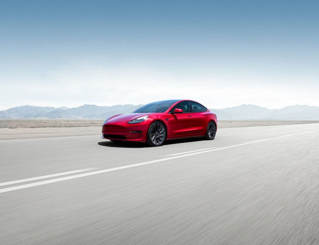 A red 2021 Tesla Model 3 driving through the mountains with a blue sky above it, the 2021 Tesla Model 3 is one of the best AWD cars of 2021