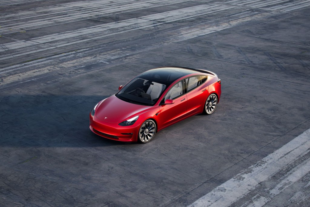 An overhead shot of a red 2021 Tesla Model 3 parked on an empty air strip
