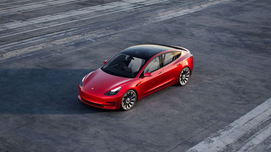 An overhead shot of a red 2021 Tesla Model 3 parked on an empty air strip