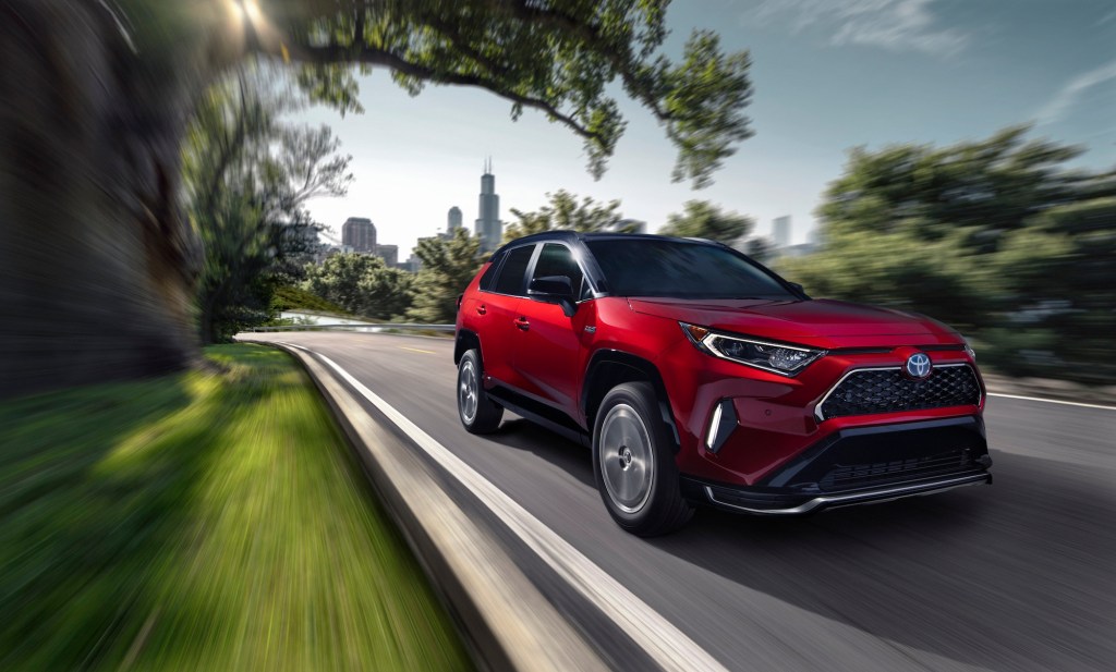 A red 2021 Toyota RAV4 Prime plug-in hybrid compact SUV traveling on a road away from a city