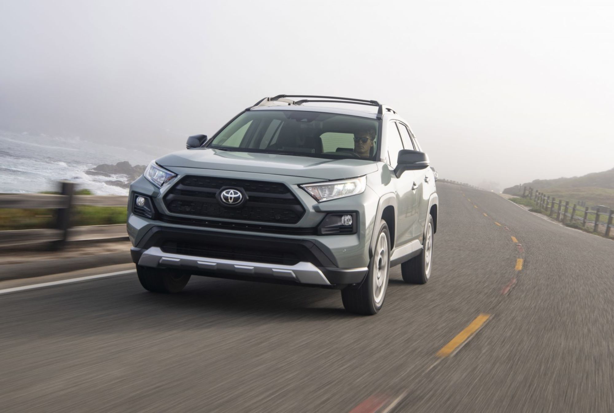 A silver 2021 Toyota RAV4 driving on a highway next to the ocean.