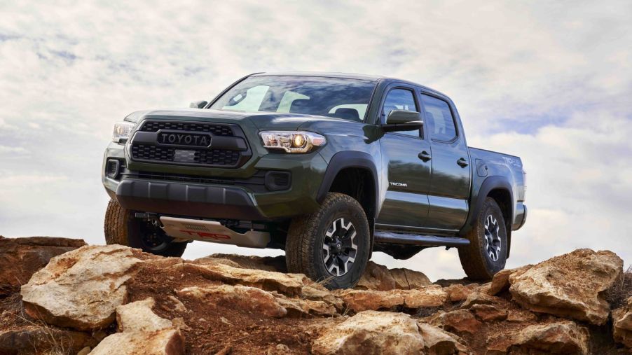 A dark green 2021 Toyota Tacoma sitting on top of a brown rocky terrain with a cloud covered background.