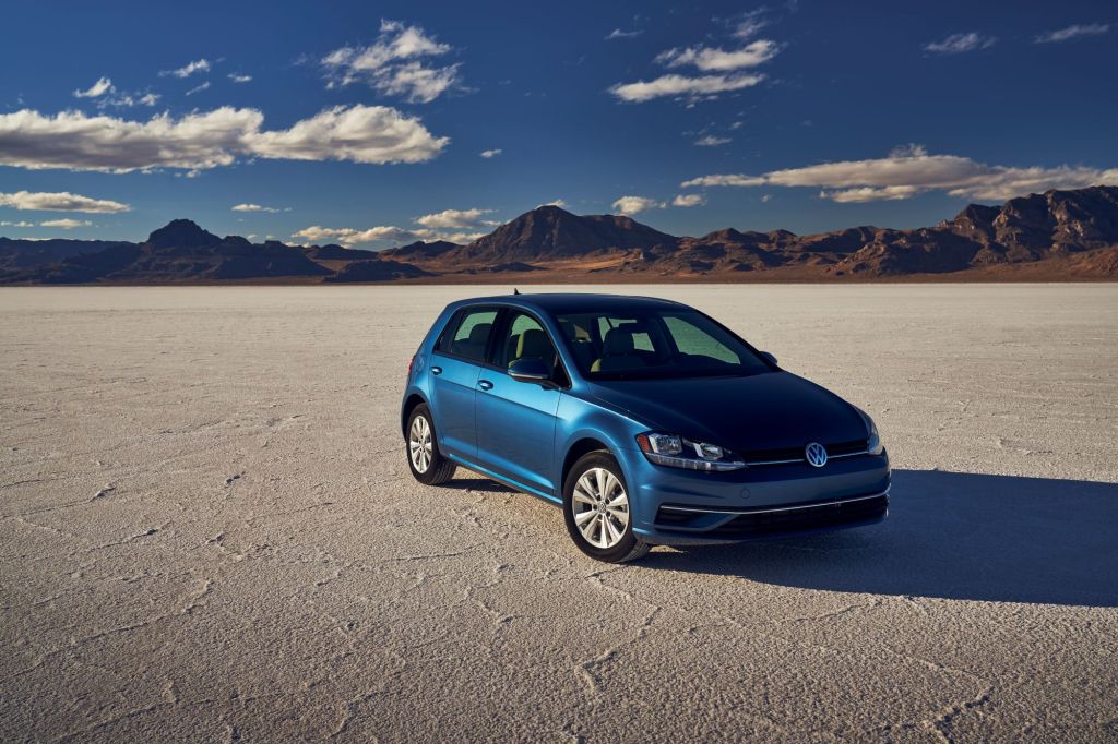 A blue 2021 Volkswagen Golf hatchback parked on a desert plain near a mountain range