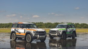 An orange-and-white and green-and-white 2022 Bowler Land Rover Defender 90 Challenge racer on a wet airstrip