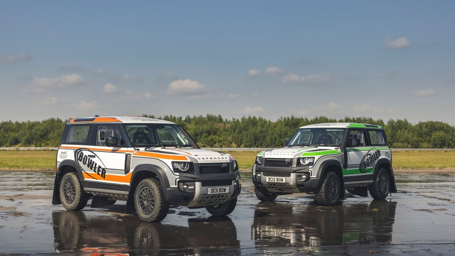 An orange-and-white and green-and-white 2022 Bowler Land Rover Defender 90 Challenge racer on a wet airstrip